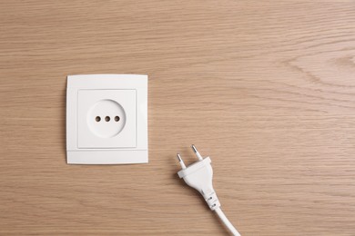 Photo of Power socket with plug on wooden table, flat lay. Space for text