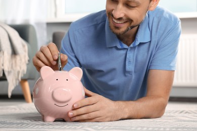 Happy man putting money into piggy bank at home, closeup