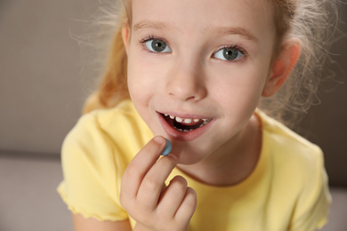 Little girl taking vitamin pill at home, closeup