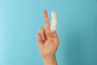 Photo of Woman with finger wrapped in medical bandage showing peace gesture on light blue background, closeup