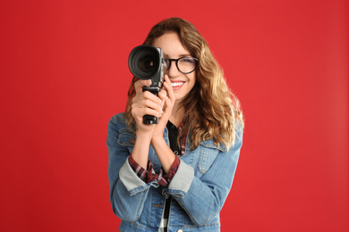 Beautiful young woman with vintage video camera on red background