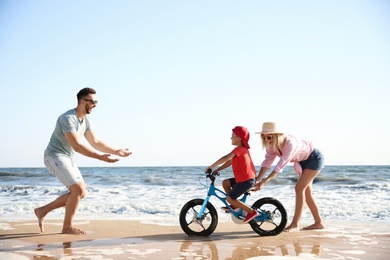 Happy parents teaching son to ride bicycle on sandy beach near sea