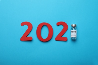 Paper numbers vial with coronavirus vaccine forming 2021 on light blue background, flat lay