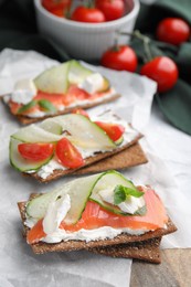 Tasty rye crispbreads with salmon, cream cheese and vegetables on parchment paper, closeup