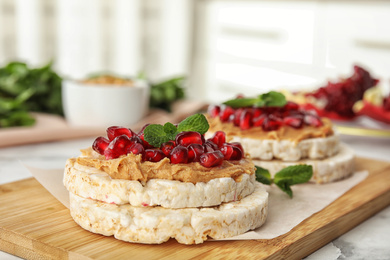 Puffed rice cakes with peanut butter, pomegranate seeds and mint on wooden board, closeup