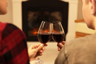 Lovely couple with glasses of wine resting together near fireplace at home, closeup