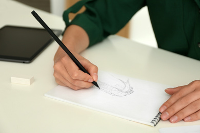 Woman drawing with pencil in notepad at white table, closeup