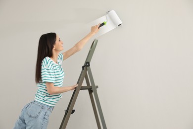 Photo of Young woman painting wall with roller on ladder, space for text