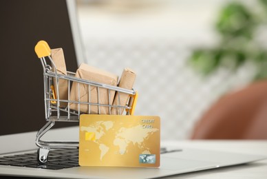 Online payment concept. Small shopping cart with bank card, boxes and laptop on table, closeup
