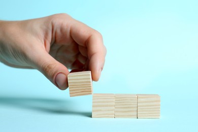 Photo of Woman arranging cubes on light blue background, closeup with space for text. Idea concept