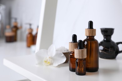 Bottles of essential oil on white shelf in bathroom. Space for text