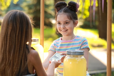 Little girl selling natural lemonade to kid in park. Summer refreshing drink