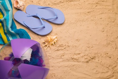 Bright beach ball, blanket, flip flops and shells on sand, flat lay. Space for text