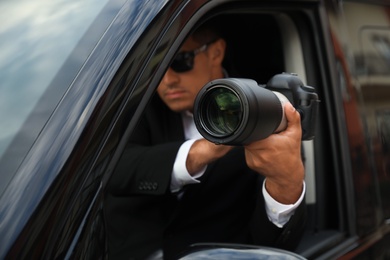 Private detective with camera spying from car, focus on lens