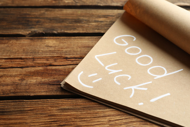 Notebook with phrase GOOD LUCK and funny face on wooden background, closeup