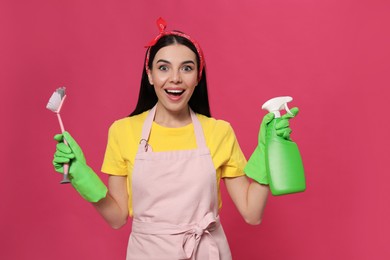 Emotional housewife with detergent and brush on pink background