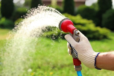 Man spraying water from hose in garden, closeup