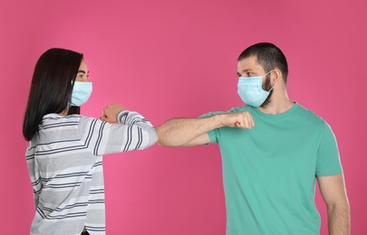 Man and woman bumping elbows to say hello on pink background. Keeping social distance during coronavirus pandemic