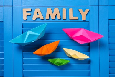 Photo of Paper ships and word Family on blue wooden background, flat lay
