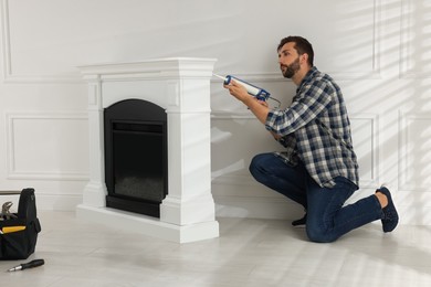 Man sealing electric fireplace with caulk near white wall in room