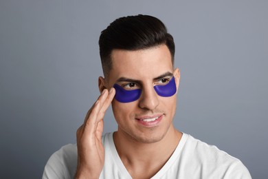 Man applying blue under eye patch on grey background