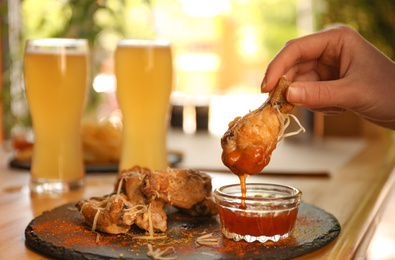 Woman dipping tasty BBQ wing into sauce at table, closeup