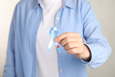 Woman holding light blue ribbon with blood drop, closeup. World Diabetes Day