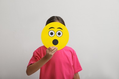 Little girl covering face with shocked emoji on white background