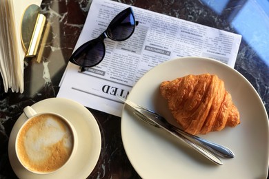 Flat lay composition with tasty croissant and cup of aromatic coffee on black table in cafeteria