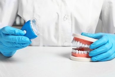 Dentist showing how to use teeth whitening device with educational model of oral cavity at table, closeup