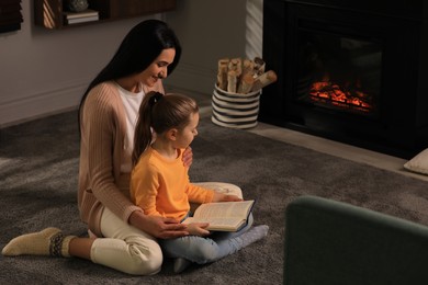 Happy mother and daughter reading together on floor near fireplace at home