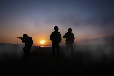 Silhouettes of soldiers with machine guns on battlefield at sunset
