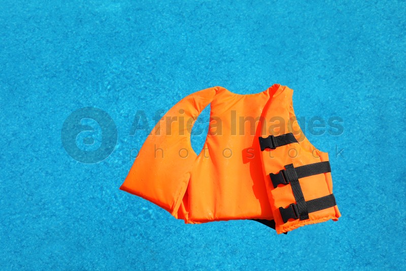 Bright orange life jacket floating in swimming pool, top view