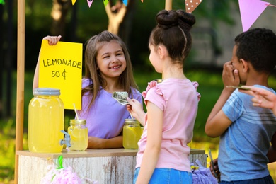 Little girl selling natural lemonade to kids in park. Summer refreshing drink