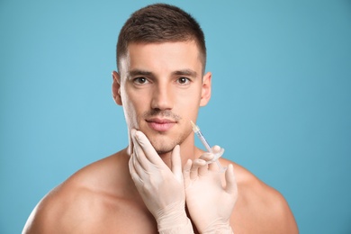 Man getting facial injection on light blue background. Cosmetic surgery