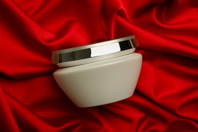 Photo of Jar of hair care cosmetic product on red fabric, top view