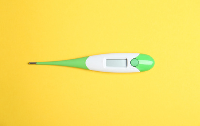 Modern digital thermometer on yellow background, top view
