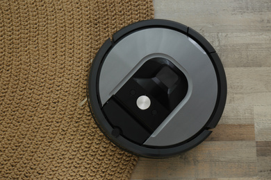 Modern robotic vacuum cleaner on knitted rug, top view