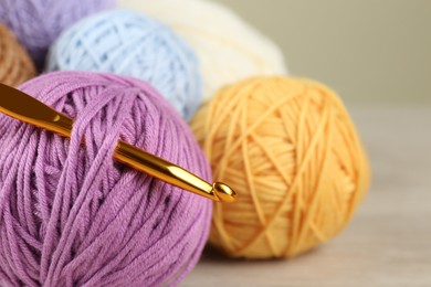 Clews of colorful knitting threads and crochet hook on wooden table, closeup