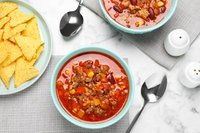 Tasty chili con carne and tortilla chips on white marble table, flat lay