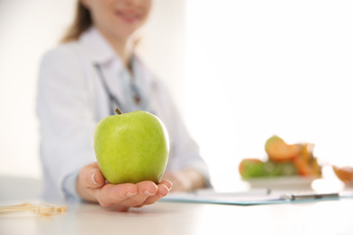 Nutritionist with apple at desk in office, closeup. Space for text