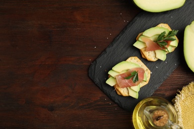Delicious crackers with avocado, prosciutto and parsley on wooden table, flat lay. Space for text