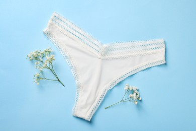 Photo of White women's underwear and flowers on light blue background, flat lay