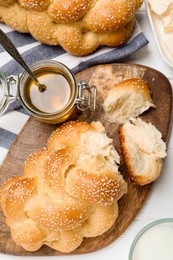 Homemade braided bread with sesame seeds, butter and honey on white wooden table, flat lay. Traditional challah