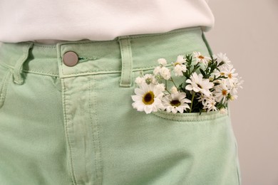 Woman with beautiful tender flowers in pocket of jeans on light background, closeup