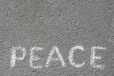 Word Peace written with white chalk on asphalt outdoors, top view. Space for text