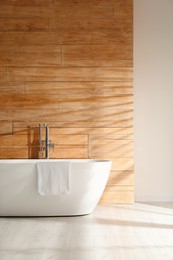 White bathtub with towel near wooden wall in room