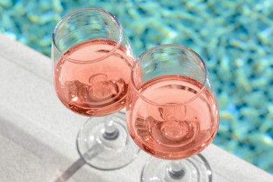 Photo of Glasses of tasty rose wine on swimming pool edge, closeup