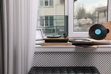 Stylish turntable with vinyl discs on windowsill in room
