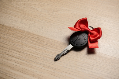 Key with red bow on wooden background, space for text. Car buying